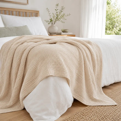 Couverture d’été Amaya beige, légère et respirante, drapée sur un lit dans une chambre lumineuse.
