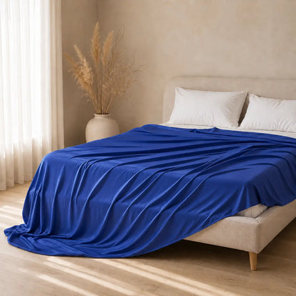 Couverture rafraîchissante Azur bleu roi en tissu effet soie glacée, drapée sur un lit beige dans une chambre minimaliste lumineuse aux tons neutres.