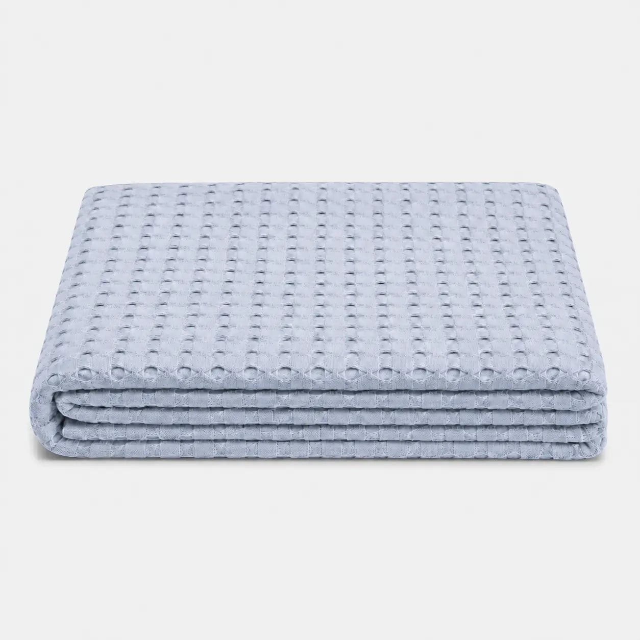 Couverture rafraîchissante Nuvia en fibre de bambou bleu, pliée sur fond clair avec texture gaufrée respirante et toucher doux.