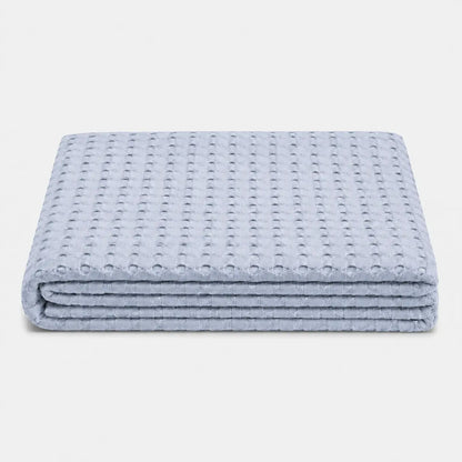 Couverture rafraîchissante Nuvia en fibre de bambou bleu, pliée sur fond clair avec texture gaufrée respirante et toucher doux.