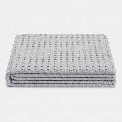 Couverture rafraîchissante Nuvia en fibre de bambou gris perle, pliée sur fond clair avec texture gaufrée respirante et toucher doux.