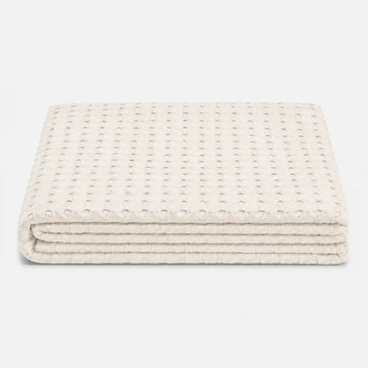Couverture rafraîchissante Nuvia en fibre de bambou ivoire, pliée sur fond clair avec texture gaufrée respirante et finition douce.