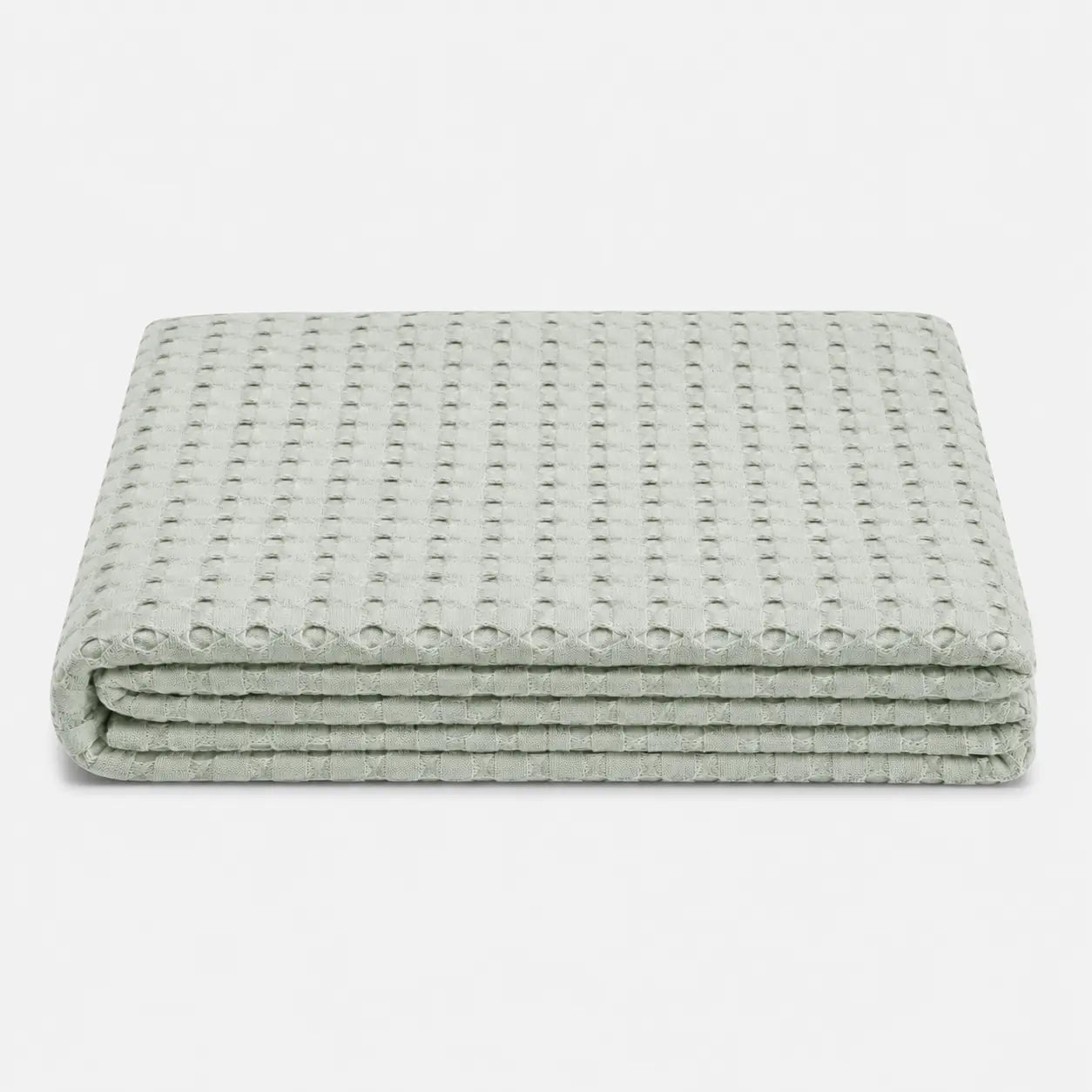 Couverture rafraîchissante Nuvia en fibre de bambou pliée, avec texture gaufrée respirante et coloris vert sauge doux sur fond clair.