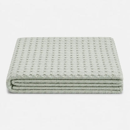 Couverture rafraîchissante Nuvia en fibre de bambou pliée, avec texture gaufrée respirante et coloris vert sauge doux sur fond clair.
